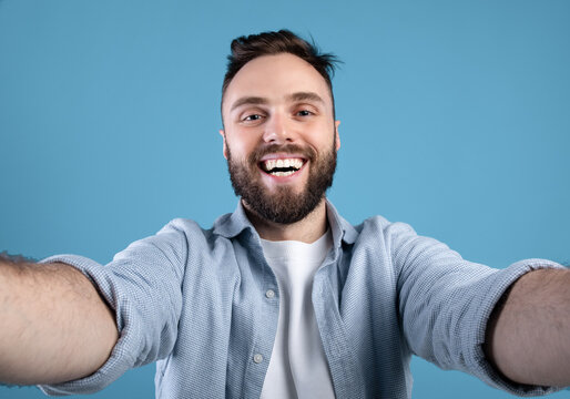 Joyful bearded guy taking selfie on blue studio background
