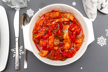 Raw herring in oil with paprika and cucumber, standing in a white plate on the Christmas table in...