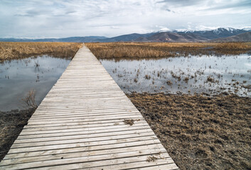 Obraz premium Moody view of bridge over a lake with marshes and snow-capped mountains in the background in Sultan Reedy National Park, central Turkey