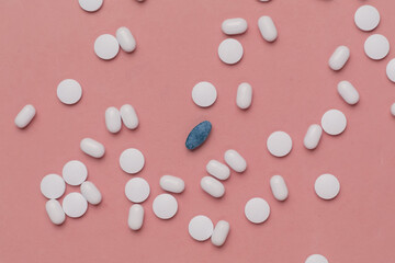 Lot of white pills and one herbal pill on pink background.