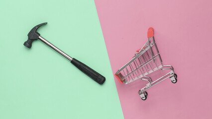Service concept, shopping. Mini shopping trolley with hammer on pink green background.