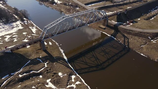 Metal railway train bridge over the river
Belarus Orsha Dnieper River. 
early spring Aerial footage from drone departing away from the bridge. downsizing landscape