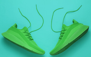 Green sport running shoes with untied laces on blue background. Top view
