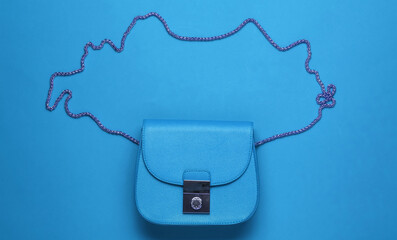 Stylish blue bag with chain on blue paper background. Top view. Minimalistic fashion concept.