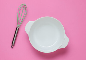 Cooking concept. Empty white bowl with whisk on pink studio background. Top view.