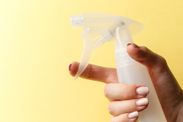 A woman's hand holds a spray bottle on bright yellow background. Natural products for cleaning or body care concept. Close-up