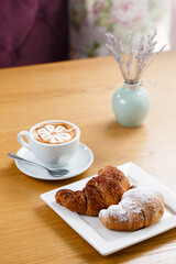 Croissants and cup of hot coffee served on the table with flowers