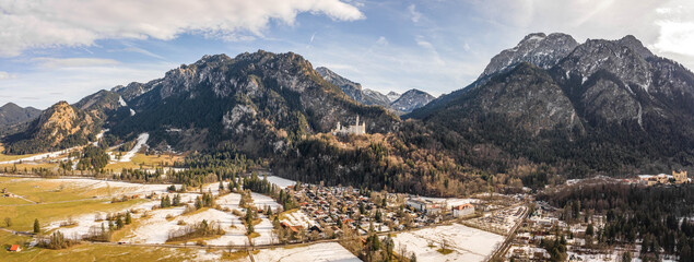 Aerial panorama drone shot of picturesque Neuschwanstein Castle on snowy hill in winter sunlight in Germany