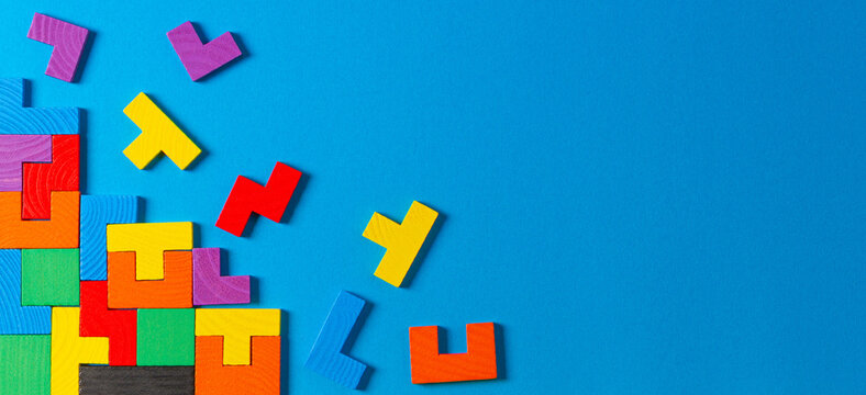 Different colorful shapes wooden puzzle blocks on light blue background. Geometric shapes in different colors, top view, copy space