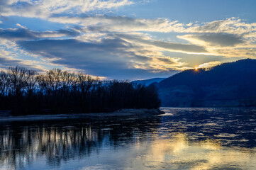 The sun disappearing behind the hills reflecting in the Danube river in Austria