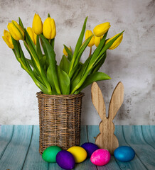 Brown vase made of willow branches with yellow tulips, in the foreground colorful Easter eggs