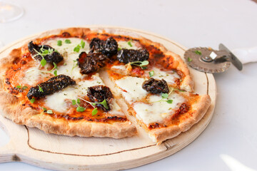 Pizza on a wooden board with mozzarella, mini arugula.