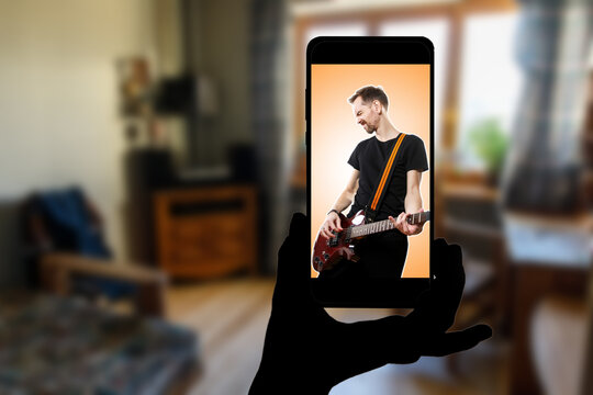 Watching online concert at home. Singer with a guitar on the screen of the smartphone