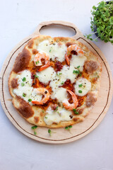 Pizza on a wooden board with mozzarella, mini arugula.