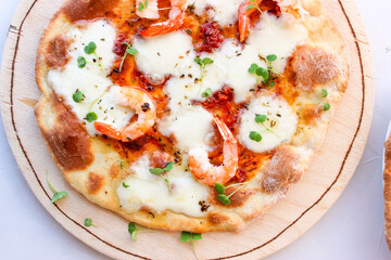 Pizza on a wooden board with mozzarella, mini arugula.
