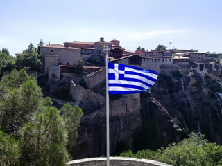 Flag of Greece is displayed against background of ancient monastery located on impregnable rock....