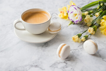 Macaroons with white cup of coffee, bright beautiful flowers on marble background.Beautiful breakfast for woman. Spring concept.Copy space