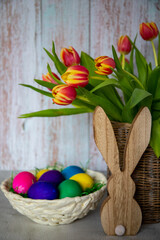 Brown vase made of willow branches with yellow-red tulips, in the foreground colorful Easter eggs