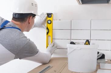 the senior master accepts the correct laying of tiles on the wall with the help of the yellow level