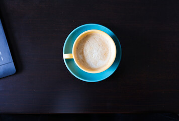 yellow cup of coffee with green saucer on dark wooden table