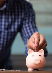Vertical business man hand putting coins into the piggy bank, saving money concept.
