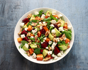Healthy Butternut squash salad with beetroot, avocado, walnut and feta cheese in white bowl