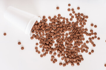 DIY homemade sweets. Home confectioner business concept. Chocolate callets scattered from a disposable cup on a white background. top view close-up. Flat lay.