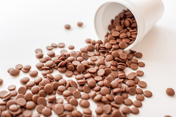 Chocolate callets scattered from a disposable cup on a white background. top view close-up. Flat lay. Home confectioner business concept. DIY homemade sweets.