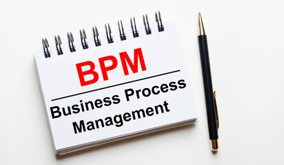 On a light background, a white notebook with are words BPM Business Process Management and a pen.