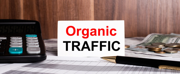On a wooden background lies pen with calculator and white card with words ORGANIC TRAFFIC