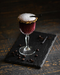 cocktail goloso in calice con granella di nocciola, caffè, vaniglia e schiuma d'uovo su tagliere nero di pietra, ardesia