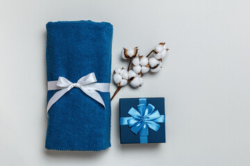 Top view of rolled blue towel with cotton sprig and gift box on gray background with copy space.