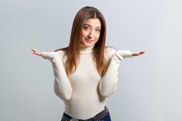 Portrait of puzzled cheerful girl showing don’t know gesture over isolated gray background. A...