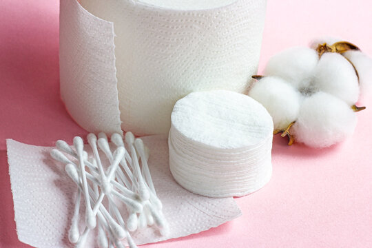 White soft cotton pads and sticks for hygiene and healthcare on light pink background.
