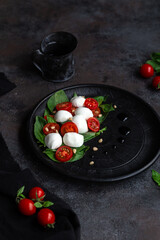 Caprese salad with mozzarella, tomatoes and basil on a black plate. Food styling
