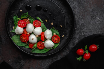 Caprese salad with mozzarella, tomatoes and basil on a black plate. Food styling
