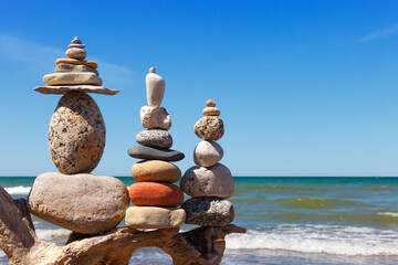 Three Rock Zen pyramid of balanced stones on a background of the summer sea and blue sky