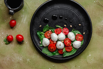 Caprese salad with mozzarella, tomatoes and basil on a black plate. Food styling