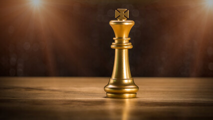 Golden king chess stand on wooden table with flare light. Winner of bussiness and successfully in the competition. Management or leadership strategy and teamwork concept.