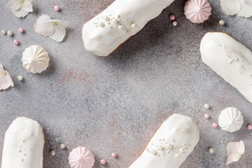 frame composition with white glaze eclairs, sweets, flowers on concrete background. Creative holiday concept with space for text. Flat lay pattern