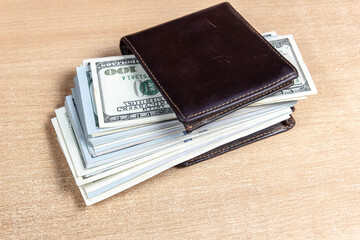 dollar bills in a brown wallet on a wooden background.