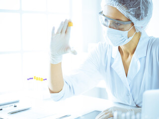 Professional female scientist in protective eyeglasses researching tube with reagents in laboratory...