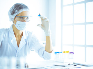 Professional female scientist in protective eyeglasses researching tube with reagents in laboratory...