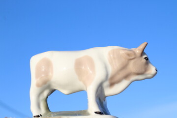 Bull Little Statuette Symbol of 2021 Year in Lunar Calendar. Horned White Spotted Cow Figurine against Clear Blue Sky
