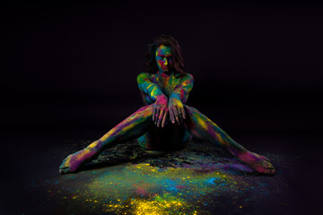 Bright colorful body art on black background, sexy nude woman painted with powder paints