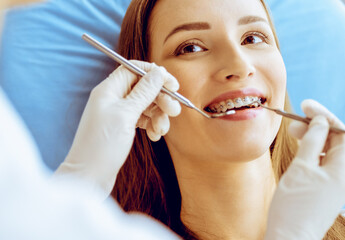 Smiling young woman with orthodontic brackets examined by dentist in dental clinic. Healthy teeth and medical care concept