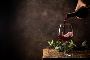 Foto auf Leinwand Rotwein in das Glas vor rustikalem dunklem Holzhintergrund gießen © petrrgoskov
