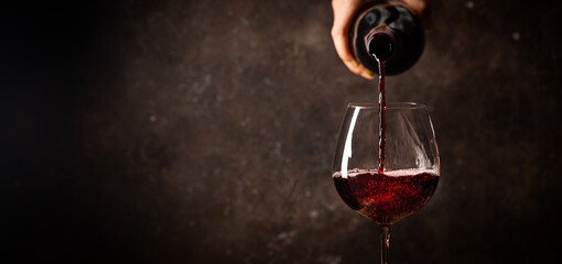 Pouring red wine into the glass against rustic dark wooden background - obrazy, fototapety, plakaty