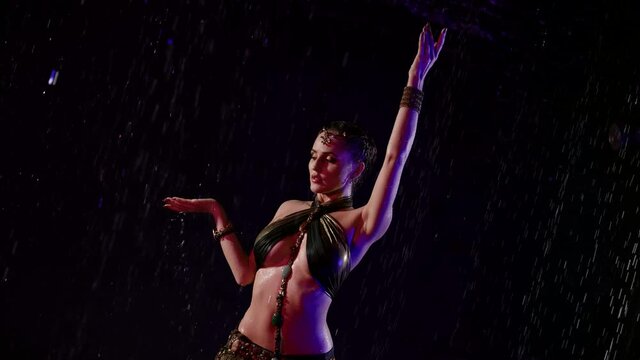 sexy arabian dancer woman is posing under rain at night, female figure in darkness