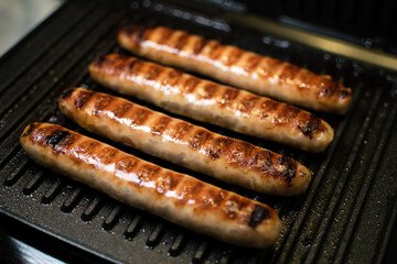 Grilled meat sausages for hot dog, kupaty, sausages, fatty food cooked on the barbecue, with fresh vegetables slicing, close-up